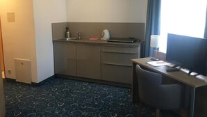Ein kleines Hotelzimmer mit einer Küchenzeile, einem Schreibtisch und einem Stuhl.