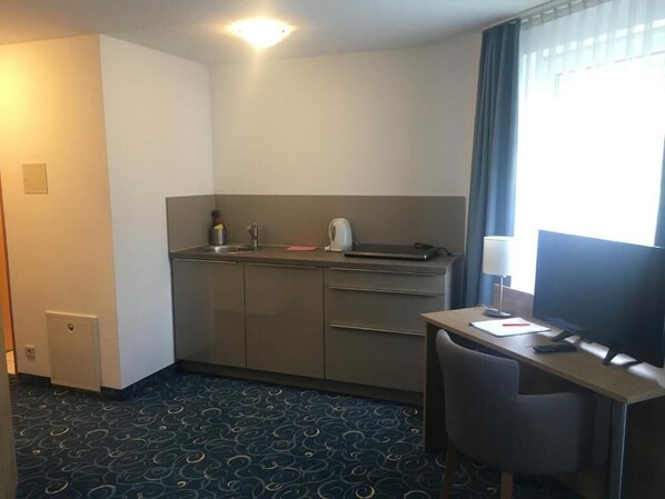 A compact hotel room with a kitchenette, a desk, and a chair. - Appartis - Hotel am Stadtpark (Sindelfingen)