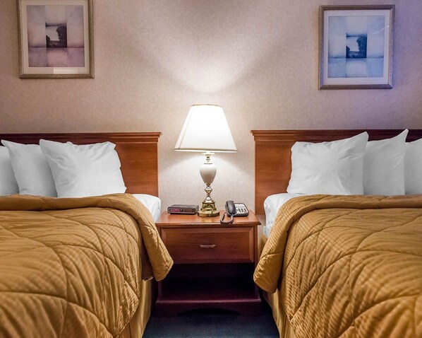 Habitación de hotel con dos camas, una mesita de noche con lámpara, teléfono y reloj digital.