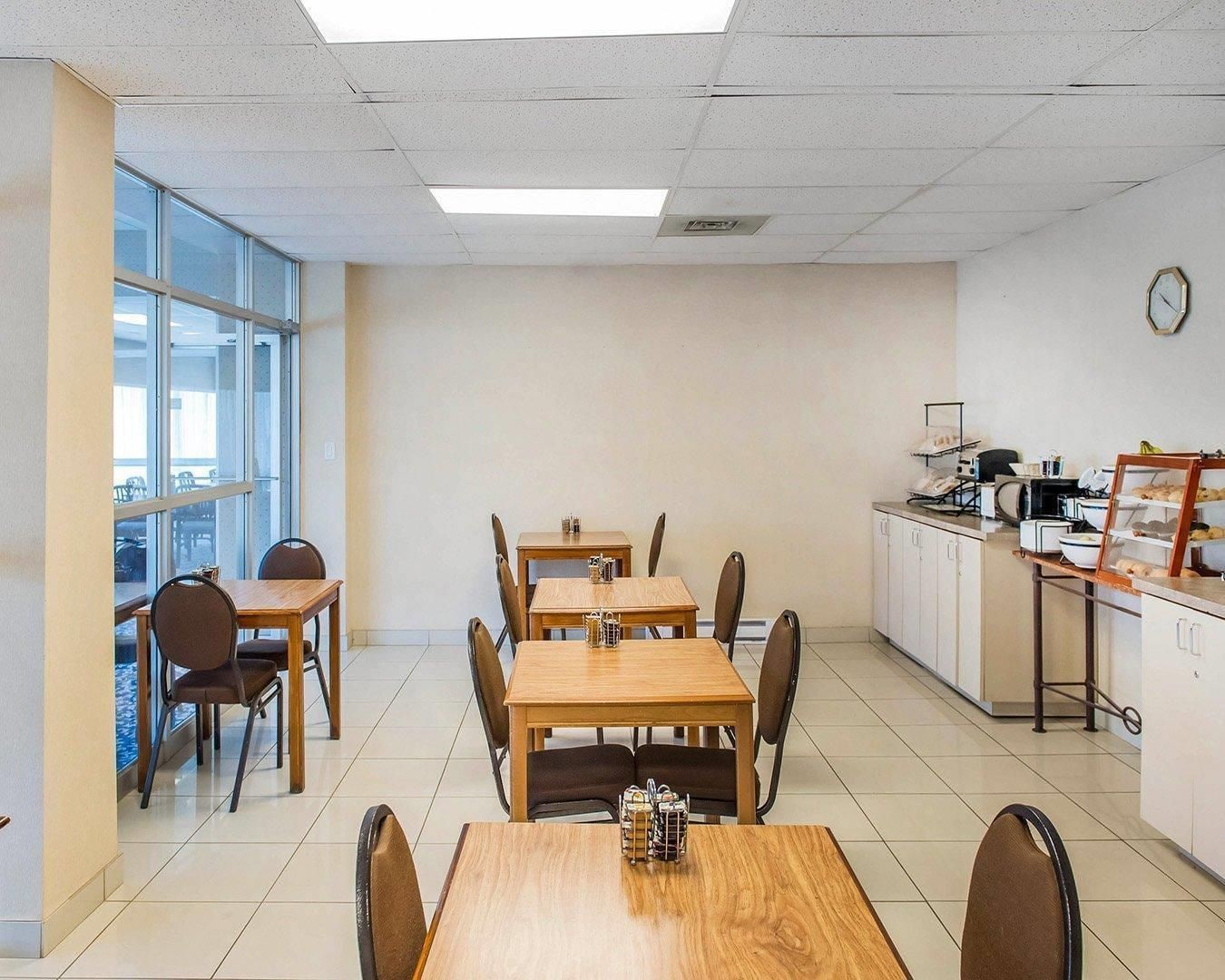 Un comedor con mesas y sillas, una zona de cocina con electrodomésticos, y un amplio ventanal que proporciona luz natural.
