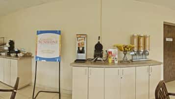 A reception area with a counter, a signboard, a coffee machine, and a vase with flowers.