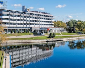 A modern building with a reflective water body in front, a clear sky, and a parking area with a few cars. - Econo Lodge Smiths Falls (Smiths Falls)
