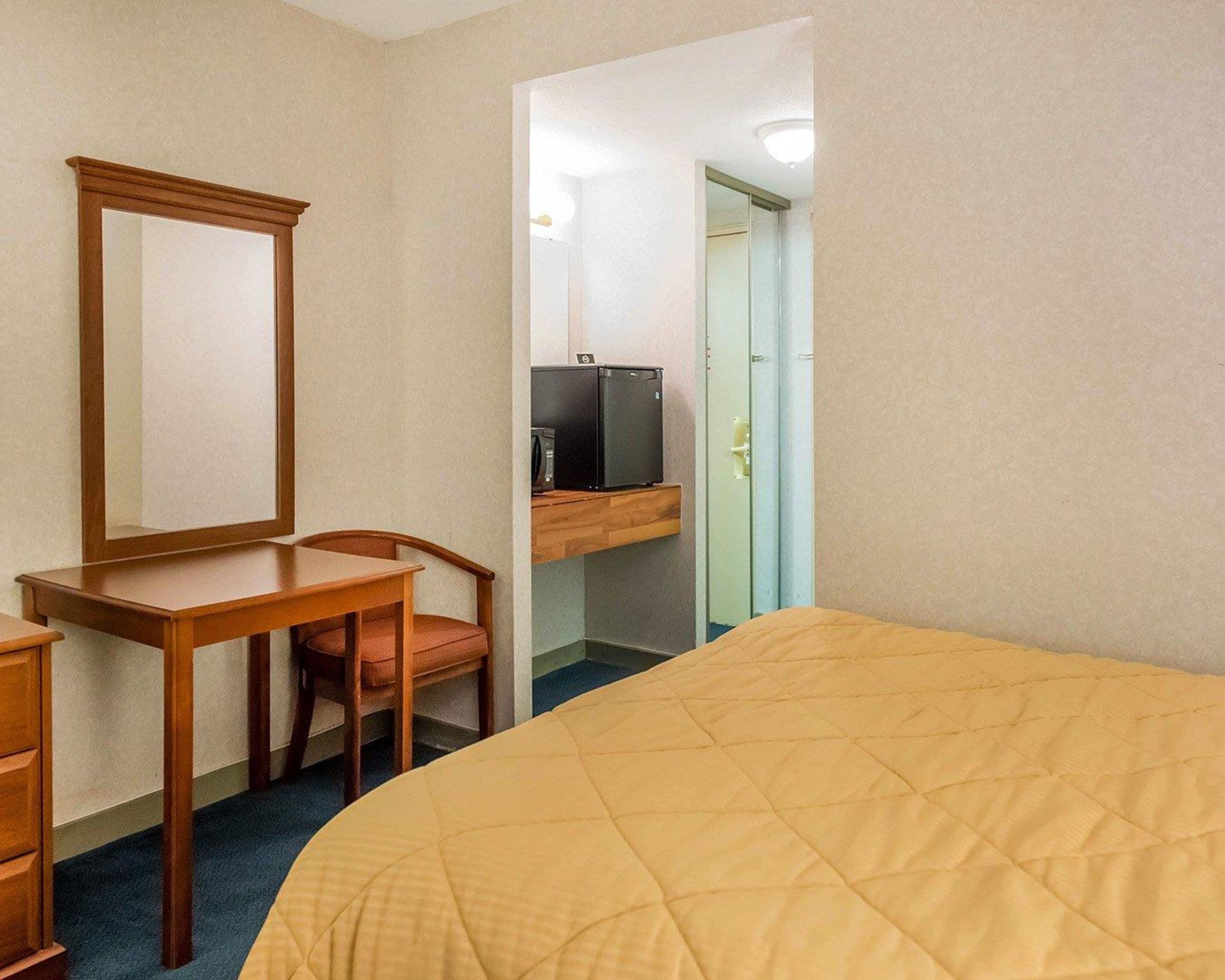 Une chambre d’hôtel comprenant un lit, un bureau avec une chaise, un miroir, une télévision et une armoire.