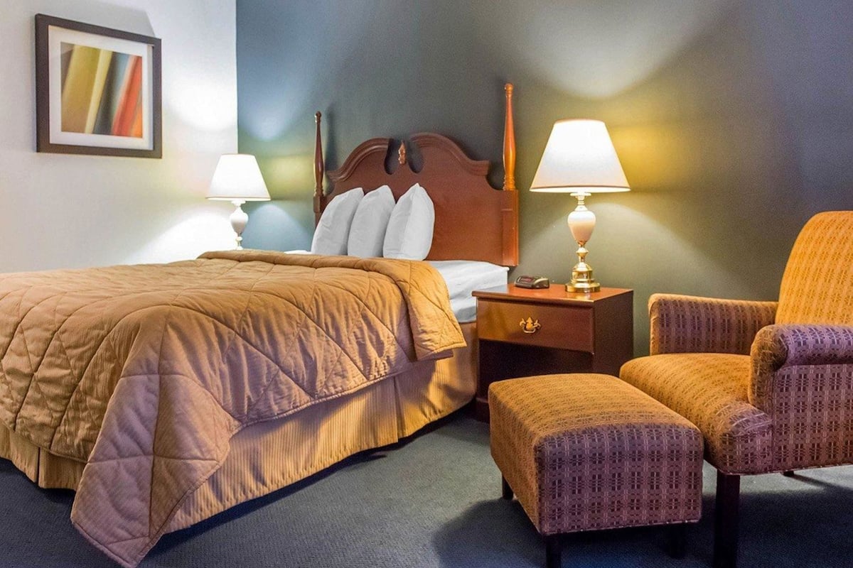 A hotel room with a bed, two bedside tables with lamps, a chair, and an ottoman.