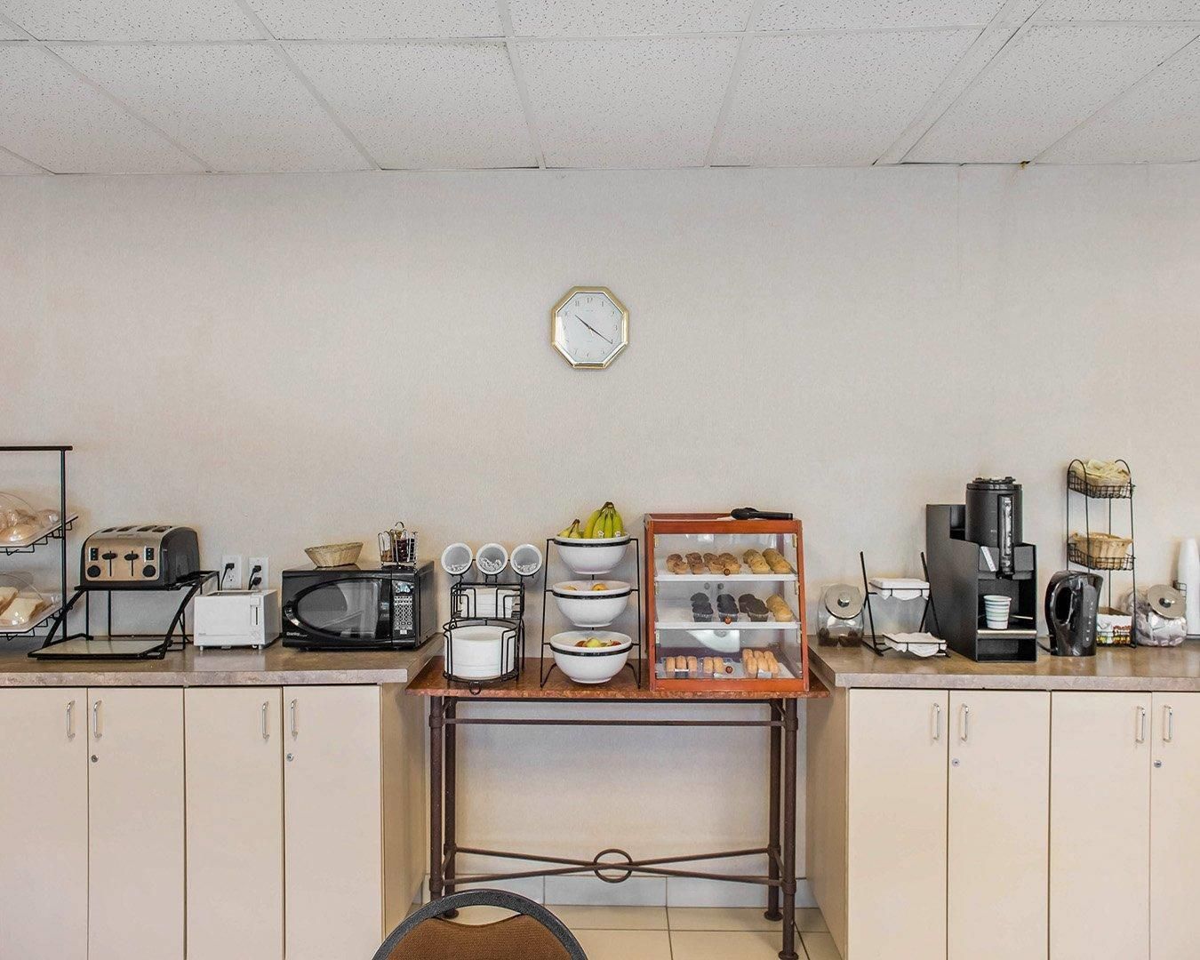 A kitchenette with a microwave, toaster, and coffee maker. There are shelves with bowls and a clock on the wall.
