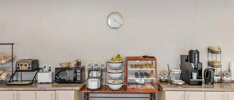 A kitchenette with a microwave, toaster, and coffee maker. There are shelves with bowls and a clock on the wall.