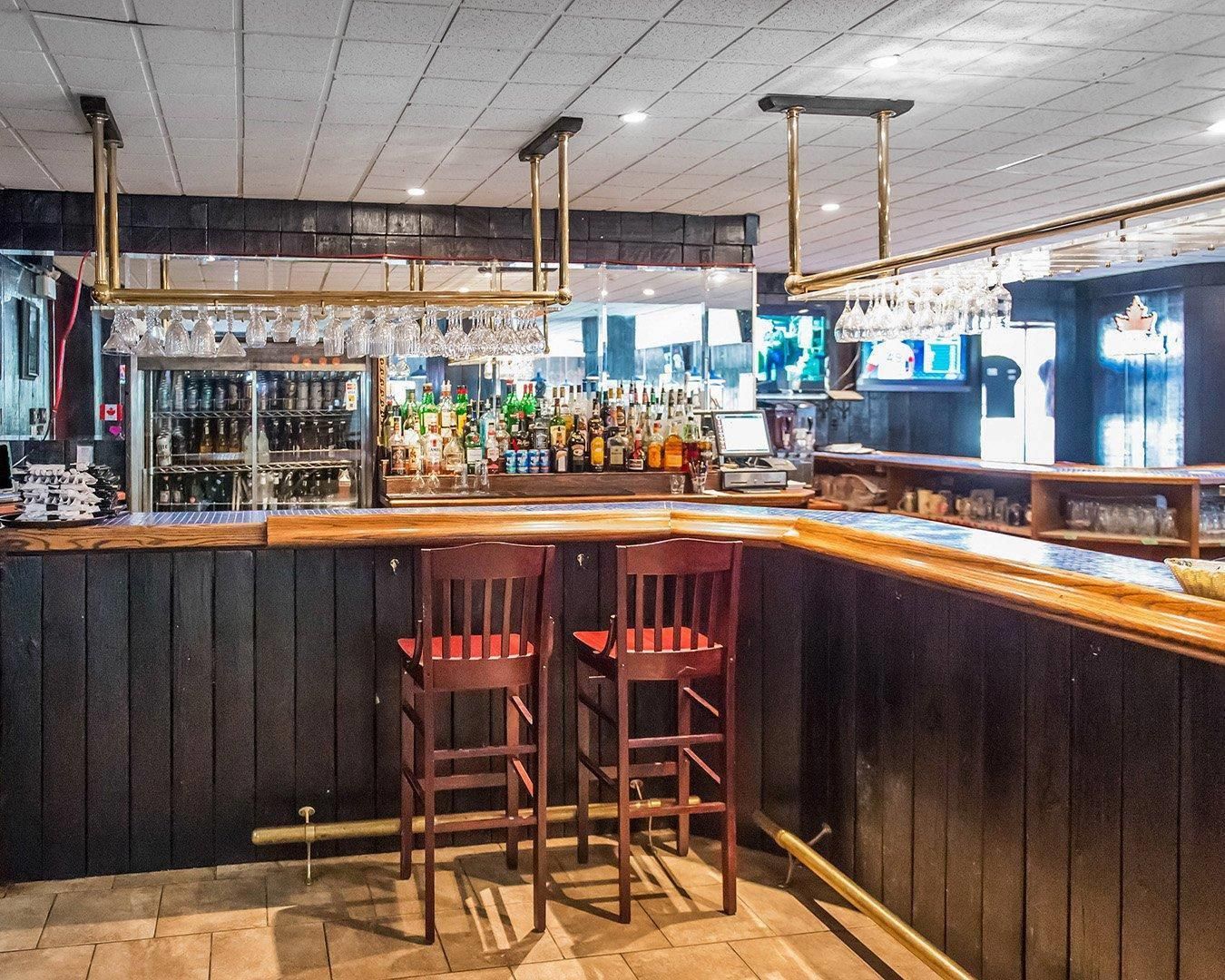 A bar area with a counter, stools, and a variety of bottles and glasses.