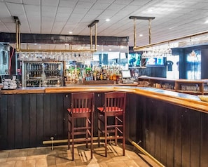 Eine Bar mit einer Theke, Hockern und einer Auswahl an Flaschen und Gläsern.