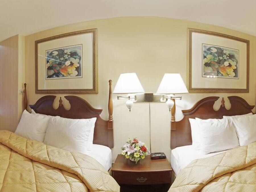 Une chambre d’hôtel avec deux lits, chacun doté d’une tête de lit en bois, de draps blancs et d’une table de chevet avec une lampe et un vase de fleurs.