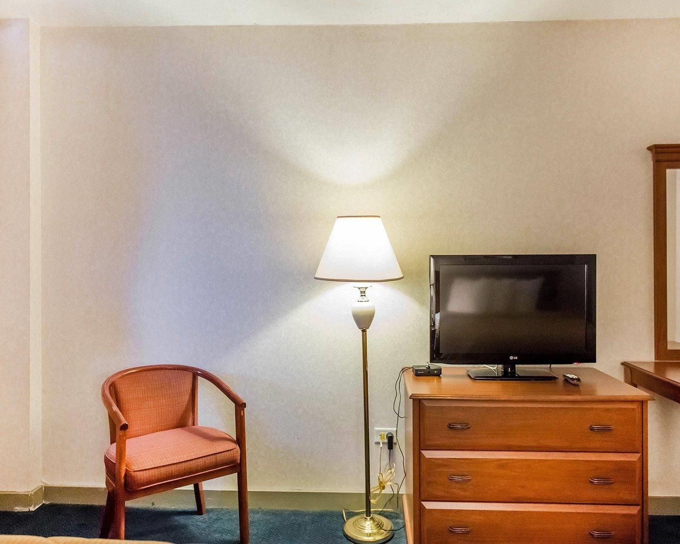 A hotel room with a wooden chair, a desk with a television, and a floor lamp.