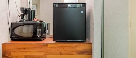 Un petit réfrigérateur et un four à micro-ondes sont posés sur une étagère en bois dans un couloir.