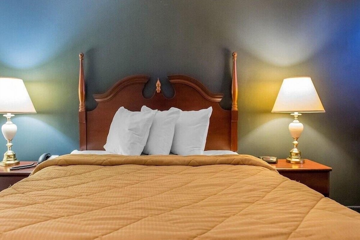 A hotel room with a large bed, two bedside lamps, and a wooden headboard.