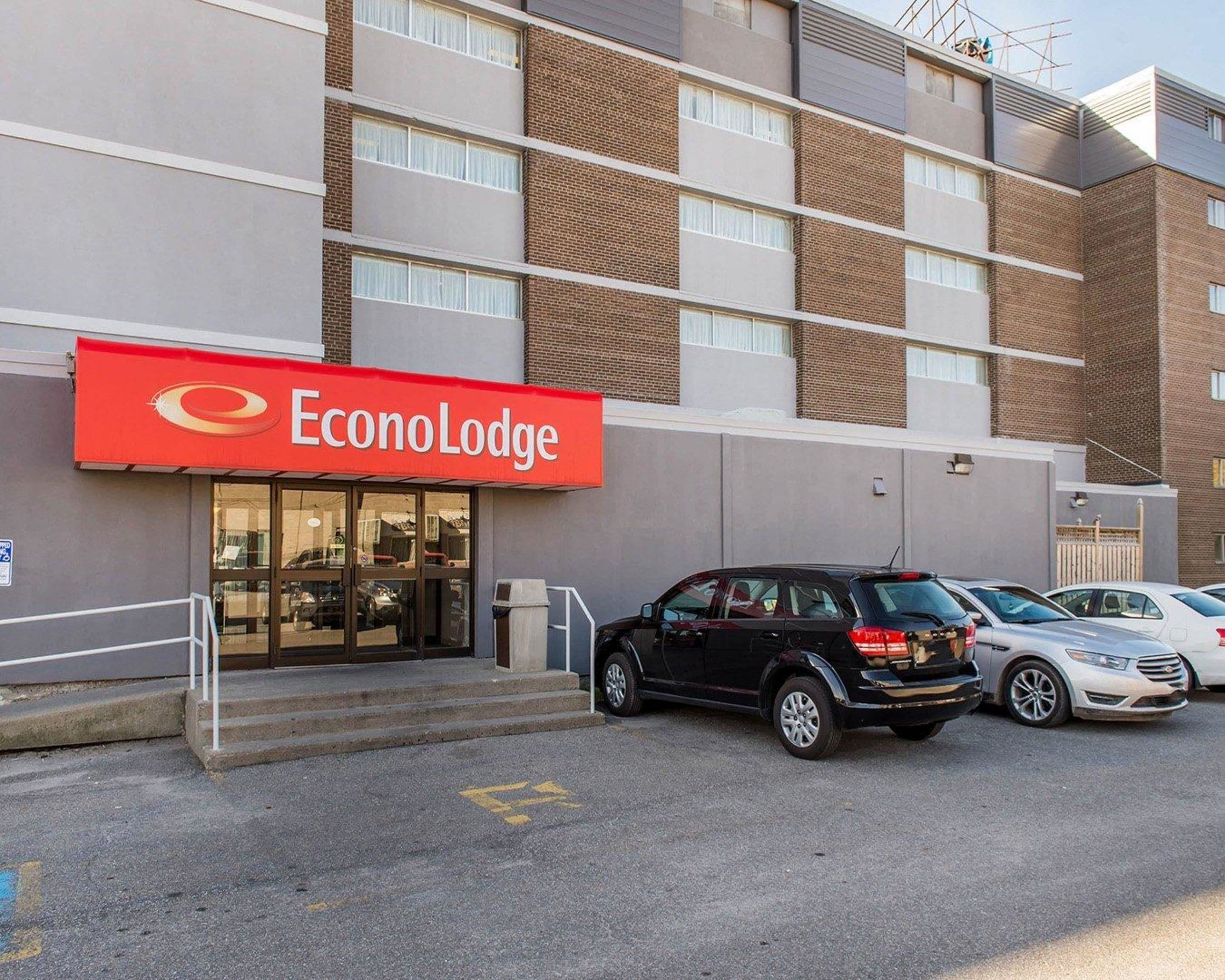 Un hotel llamado EconoLodge con un toldo rojo, un estacionamiento con varios coches y una fachada de ladrillo.