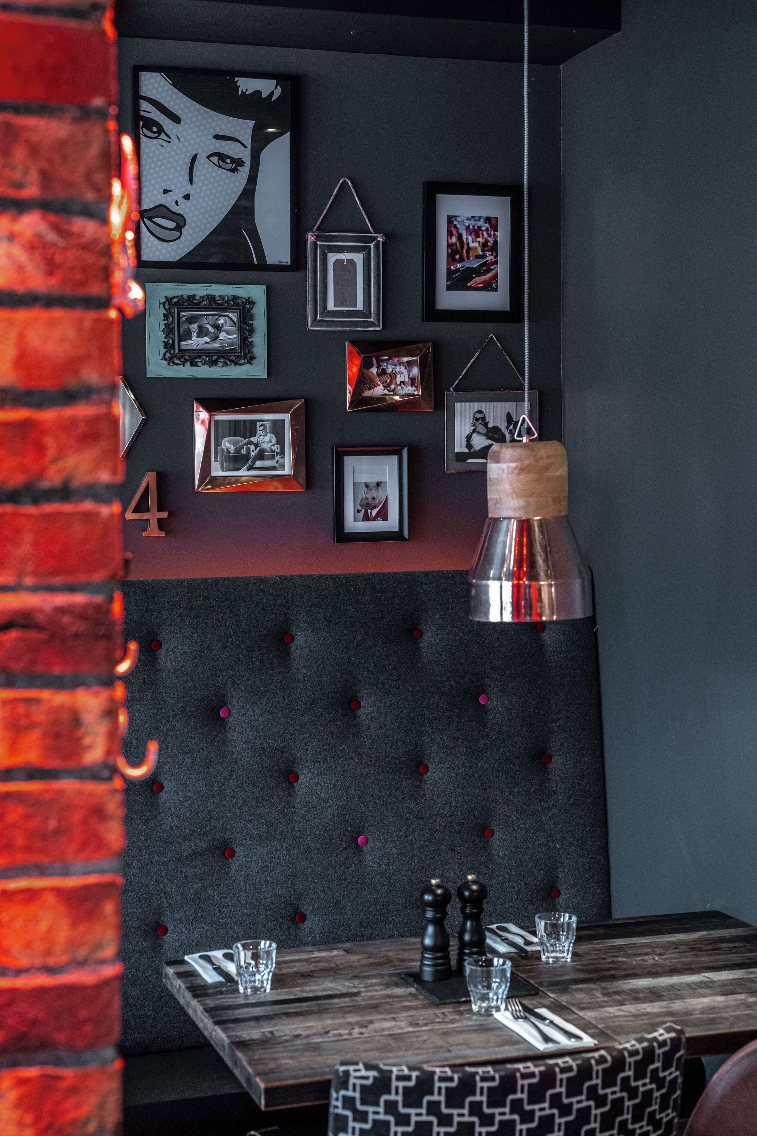 A dining area with a tufted headboard, framed pictures on the wall, and a hanging pendant light.