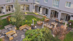A courtyard with outdoor seating, a small garden, and a building with multiple windows and doors. - pentahotel Paris Charles de Gaulle Airport (Roissy-en-France)