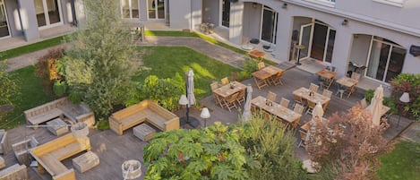 A courtyard with outdoor seating, a small garden, and a building with multiple windows and doors.