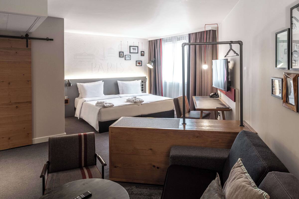 A modern hotel room with a large bed, a wooden desk, a sofa, and a TV.
