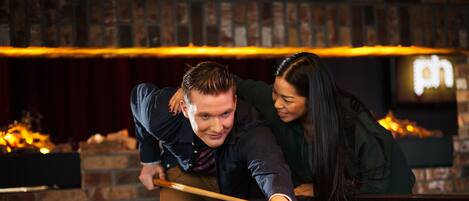 A billiards table with balls and a cue stick, set against a brick wall with a fireplace.