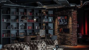 A cozy reading nook with a leather sofa, a bookshelf filled with books, and a brick fireplace. - pentahotel Paris Charles de Gaulle Airport (Roissy-en-France)