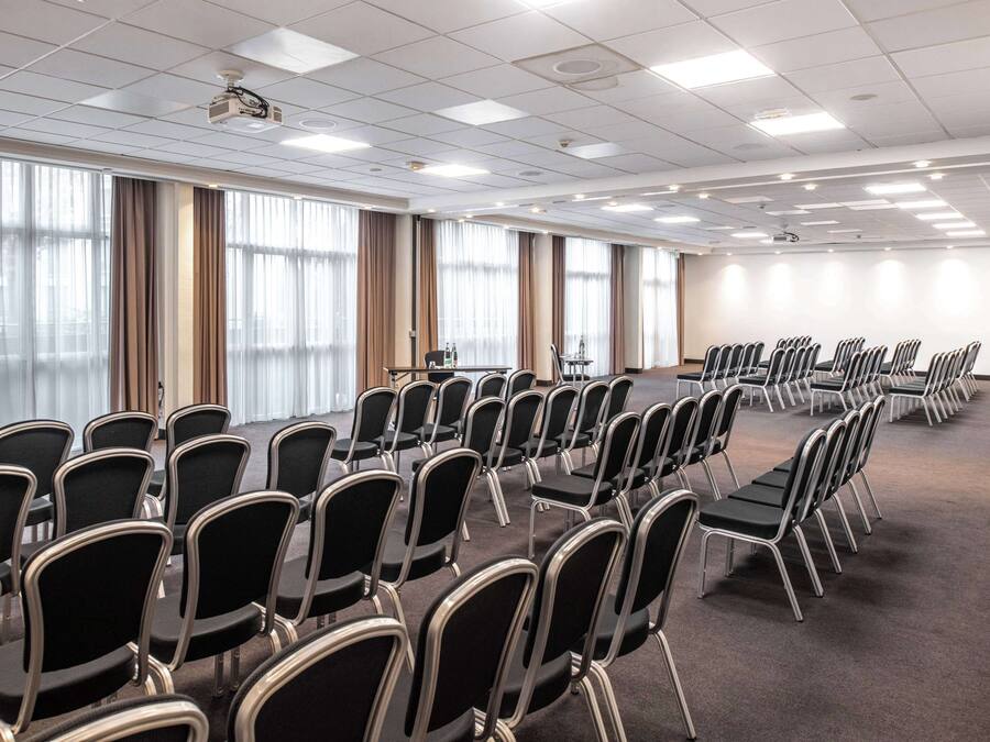 A conference room with rows of chairs, a projector, and large windows with curtains.