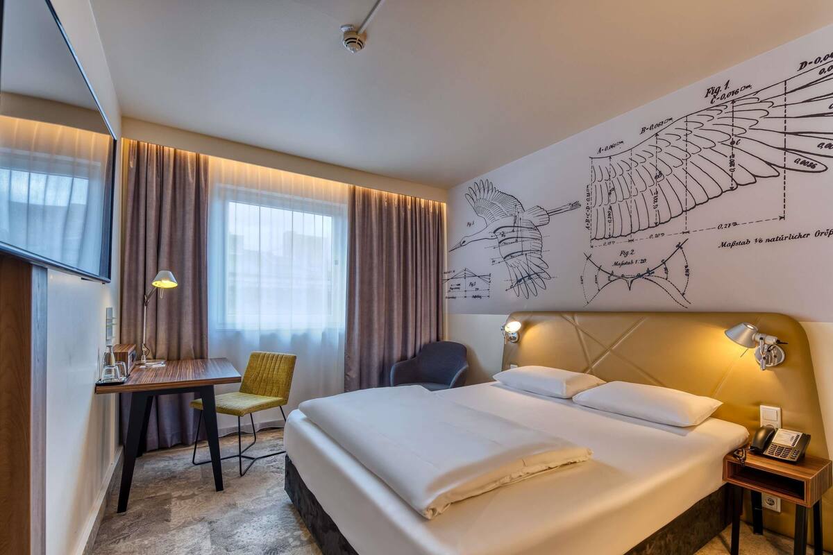 A hotel room with a bed, desk, chair, and a wall map.