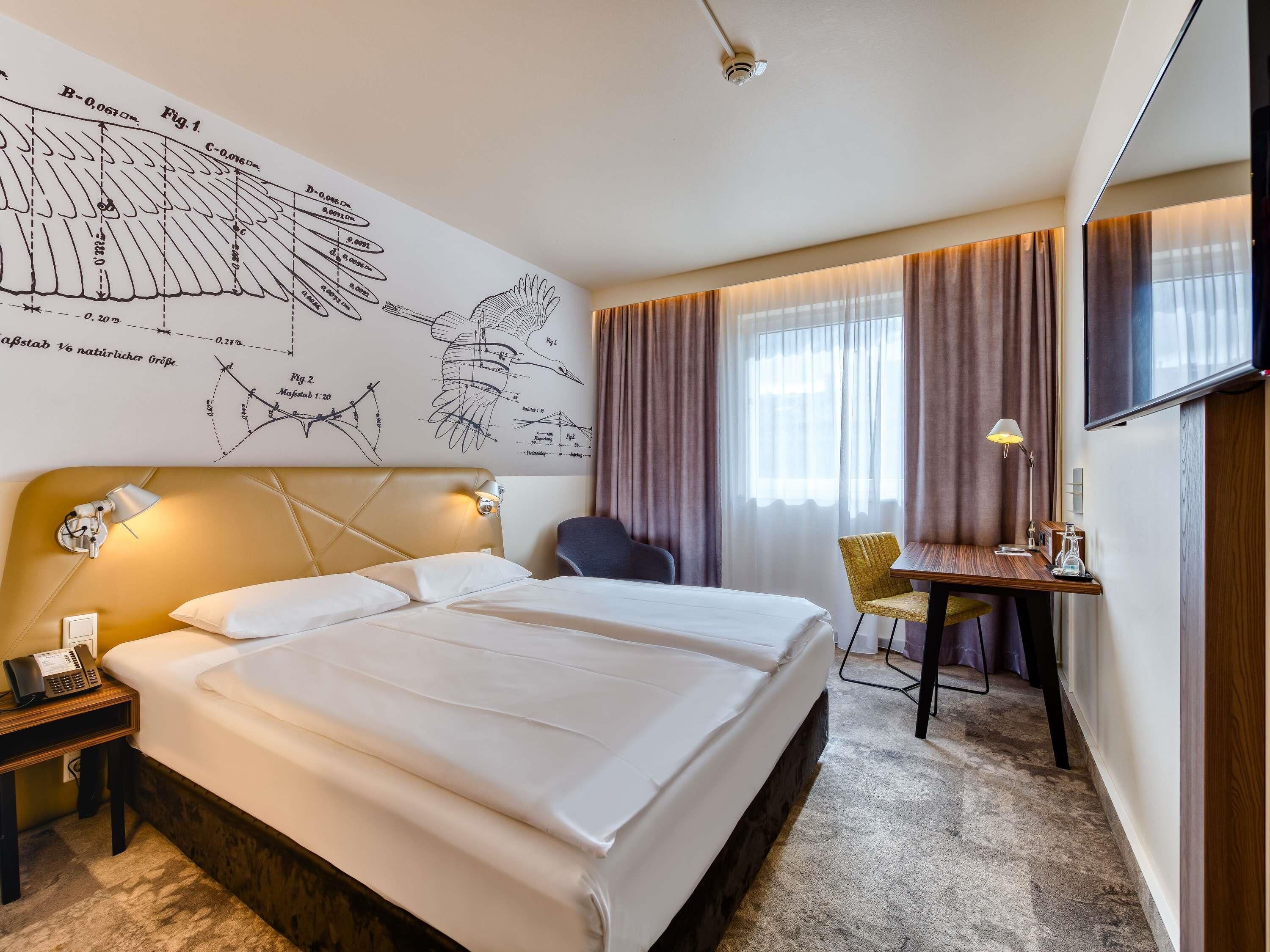 Ein Hotelzimmer mit einem großen Bett, einem Schreibtisch mit Stuhl, einem Fernseher und einer Wand mit Diagrammen.