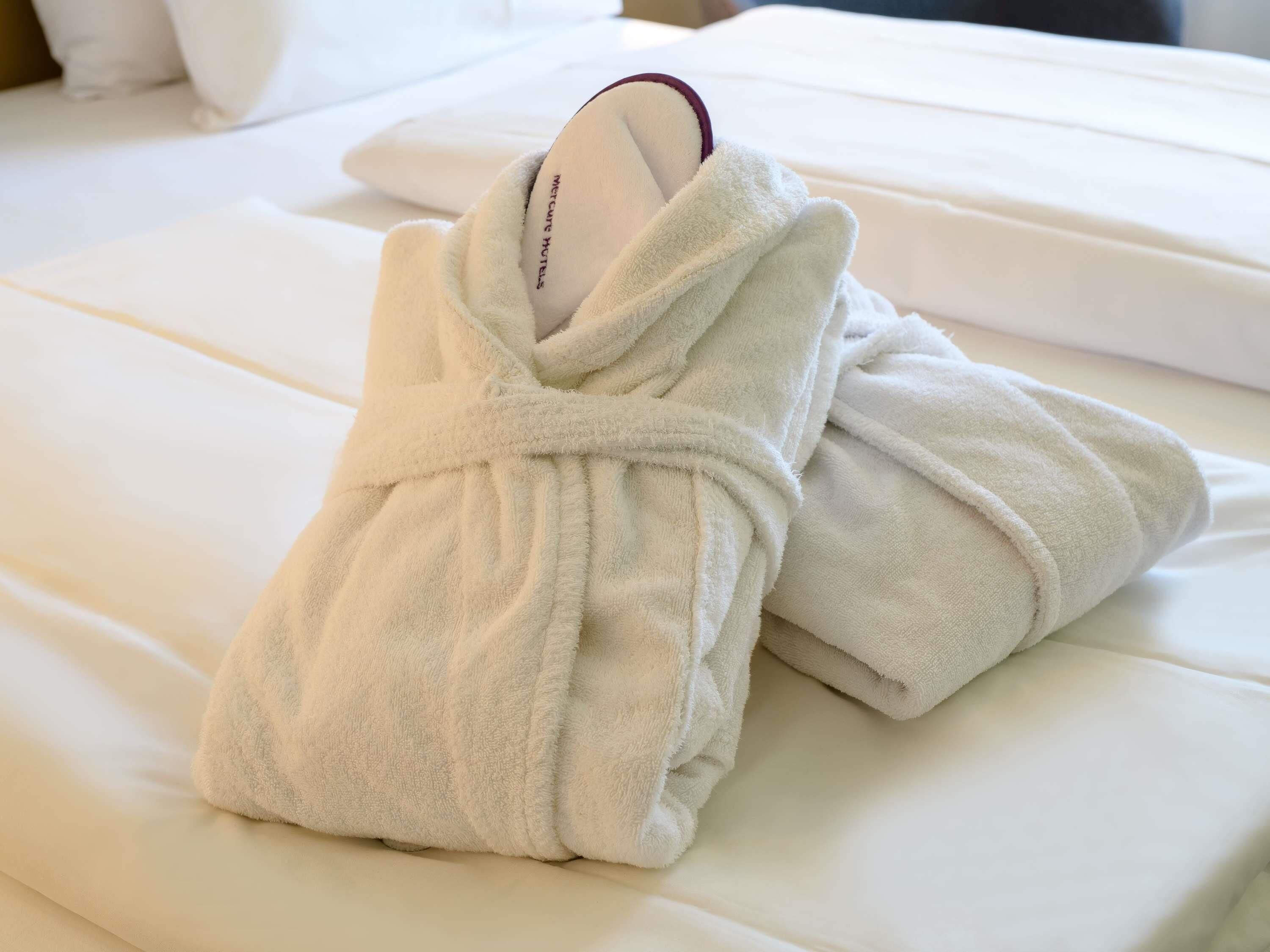 Un albornoz blanco ordenado sobre una cama con una almohada blanca y un colchón blanco.