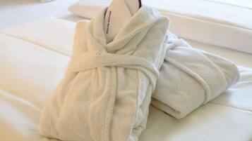 Un albornoz blanco ordenado sobre una cama con una almohada blanca y un colchón blanco.