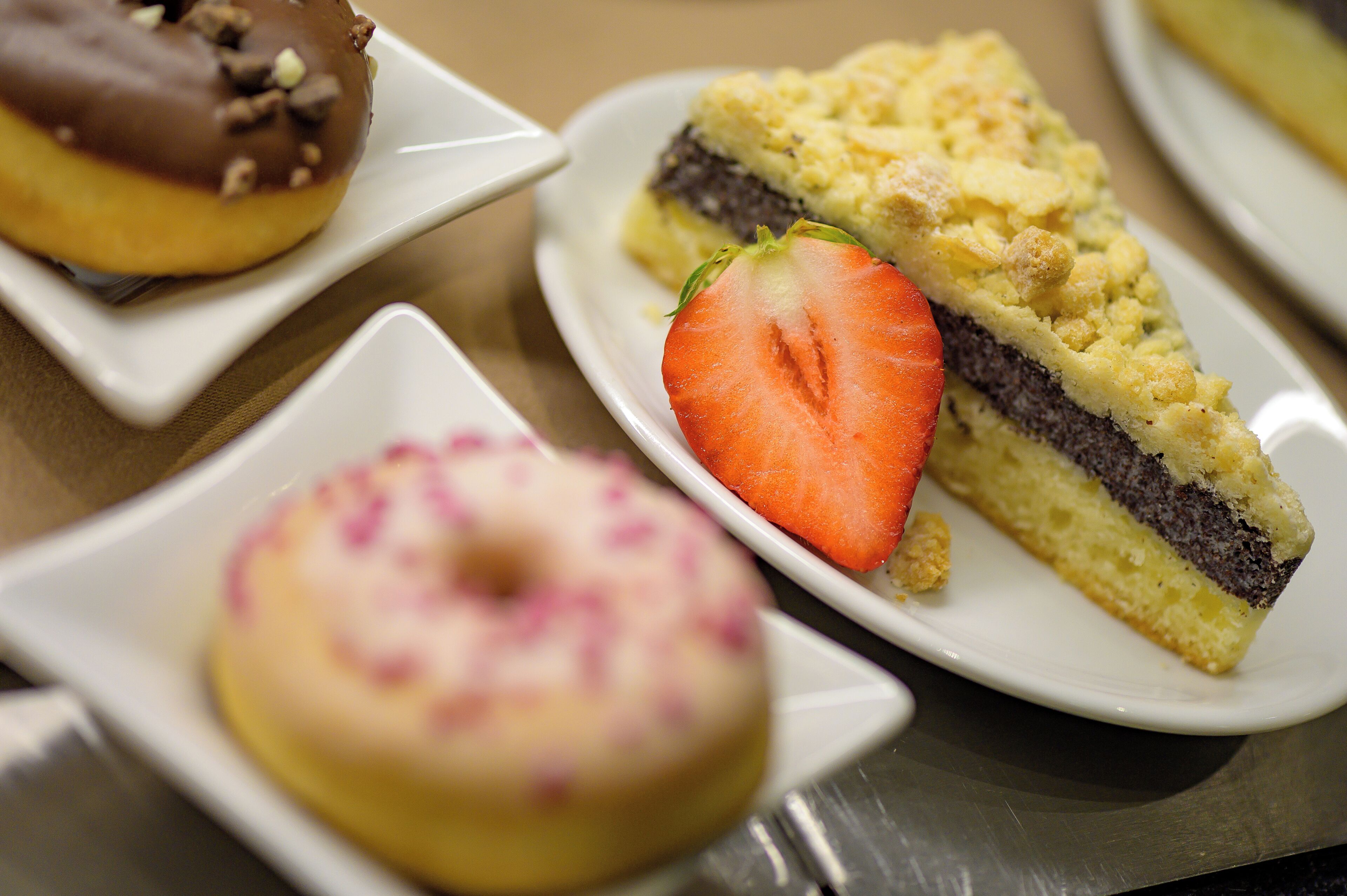 Variedad de postres en platos, incluyendo un donut cubierto de chocolate, una porción de pastel con fresa y un donut sencillo.