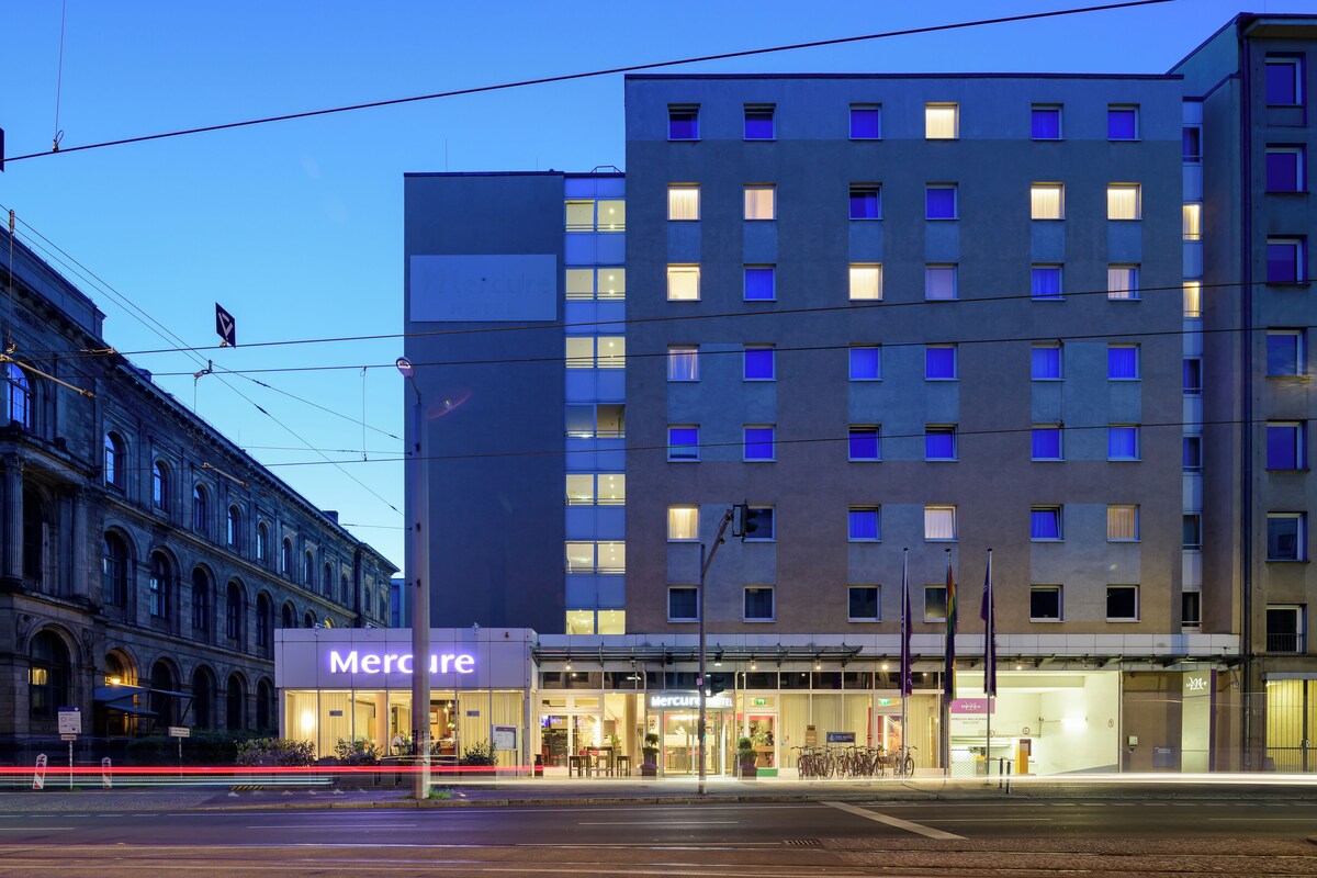Ein modernes Hotel mit einem gut sichtbaren 'Mercure'-Schild, das eine klassische Fassade und einen zeitgemäßen oberen Bereich mit gleichmäßig beleuchteten Fenstern aufweist.
