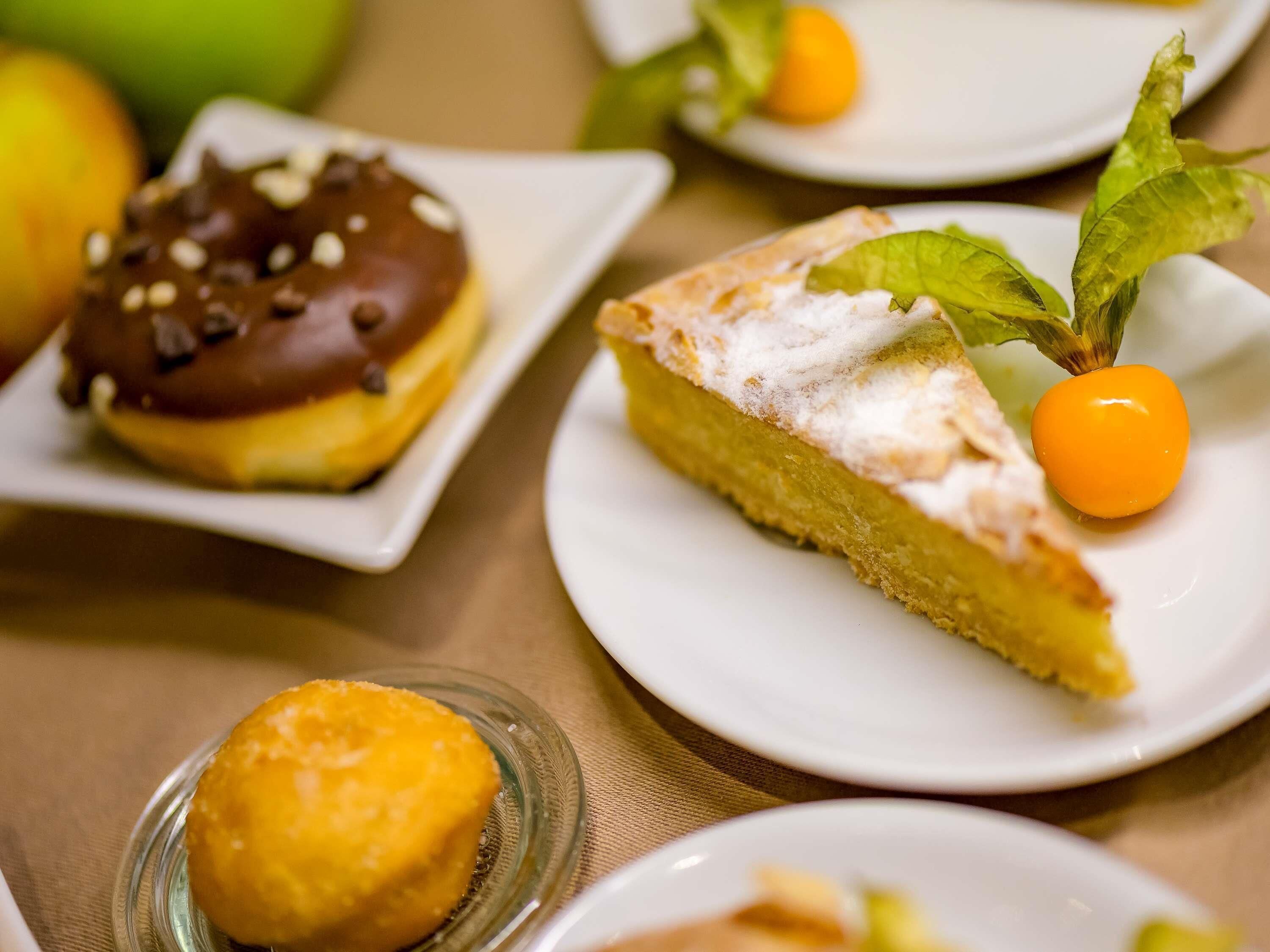 A dessert plate with a slice of cake, a small round pastry, and a cherry on a leaf.
