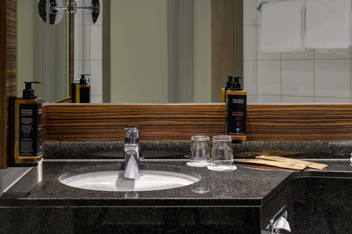 Ein Badezimmer mit Granitwaschtisch, einem Waschbecken, einem Spiegel und zwei Körperlotionflaschen.