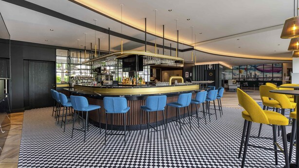 A modern bar area with a checkered floor, bar stools, and a counter with a glass display. - Mercure Neu-Isenburg (Neu-Isenburg)