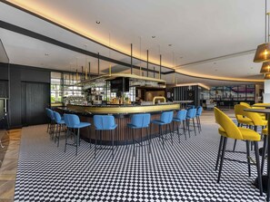 A modern bar area with a checkered floor, bar stools, and a counter with a glass display. - Mercure Neu-Isenburg (Neu-Isenburg)