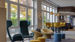 A modern lounge area with large windows, comfortable seating, and a visible departure lounge sign. - Mercure Neu-Isenburg (Neu-Isenburg)