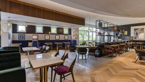 A modern restaurant interior with wooden herringbone flooring, a mix of seating including tables and booths, and large windows providing natural light. - Mercure Neu-Isenburg (Neu-Isenburg)