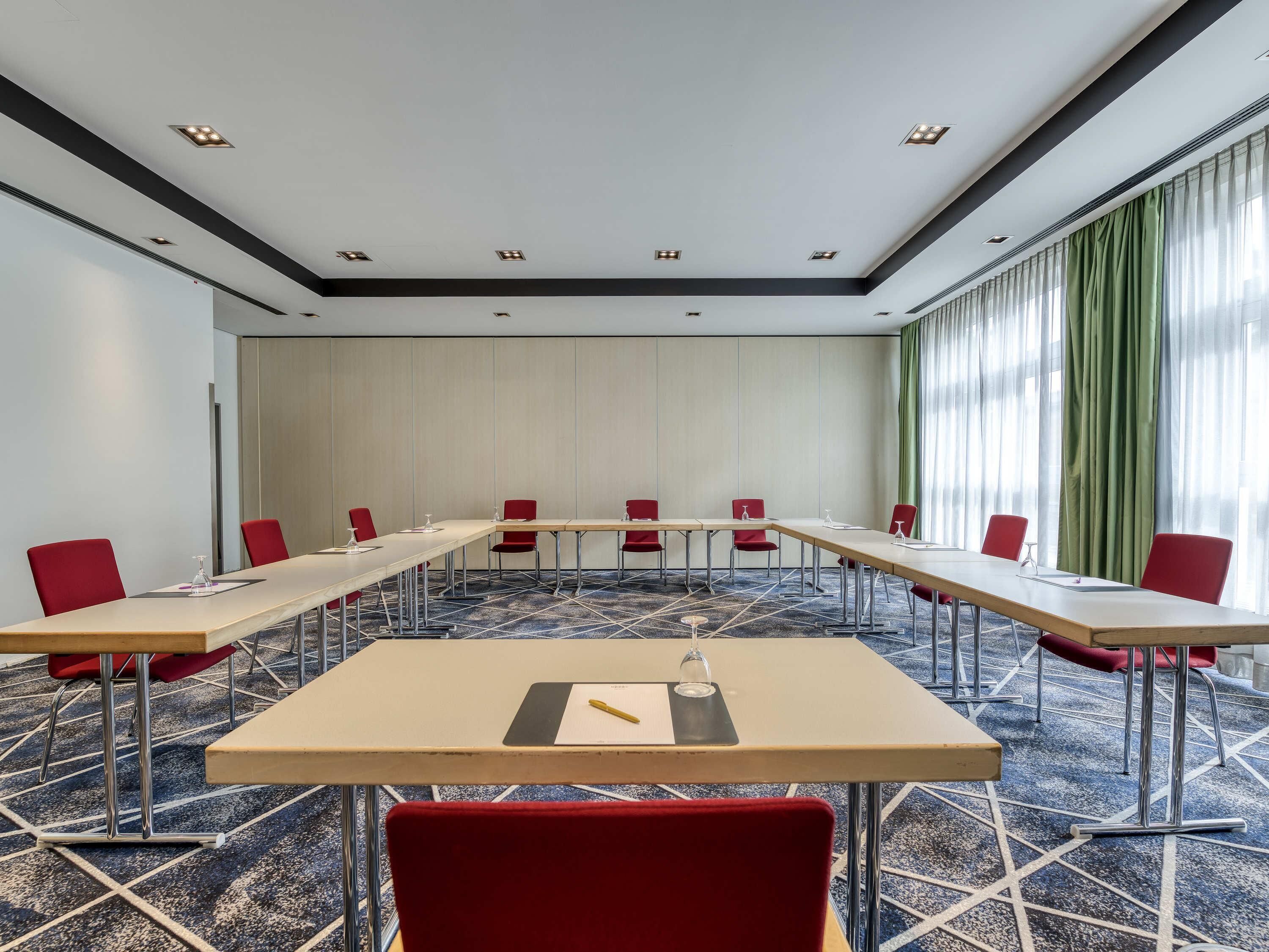 A conference room with a long table, red chairs, and a carpeted floor.