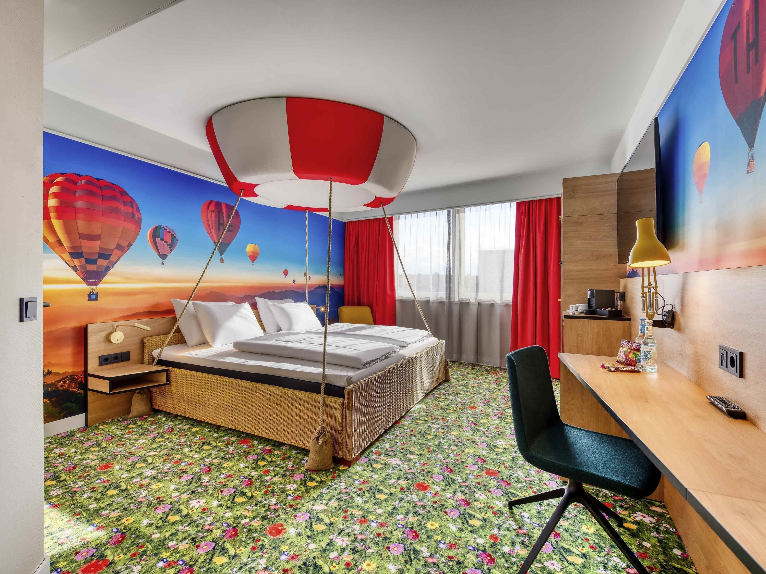 A hotel room with a bed, desk, chair, and a wall mural of hot air balloons.