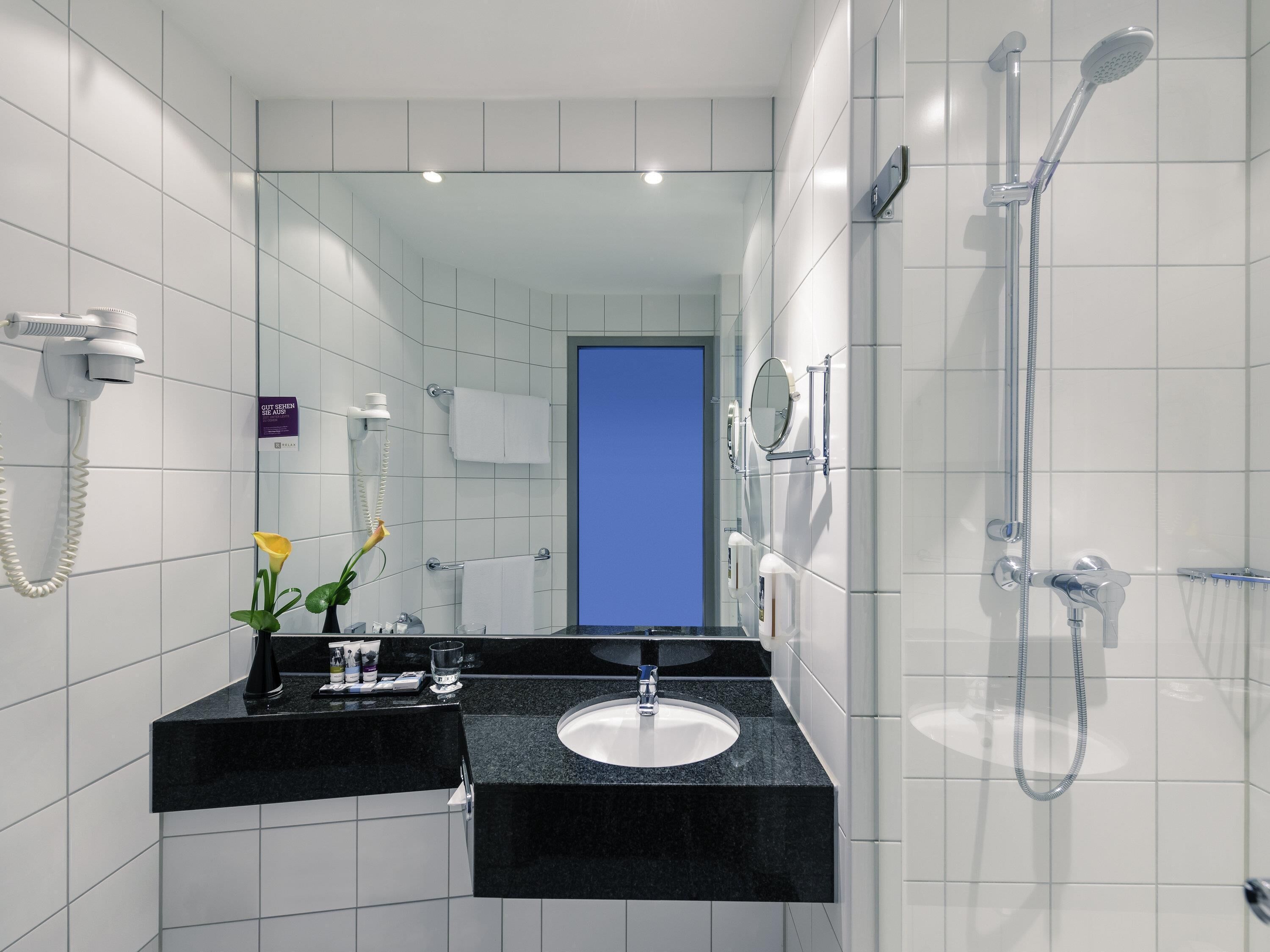 A modern bathroom with a black countertop sink, a handheld showerhead, and a mirror.