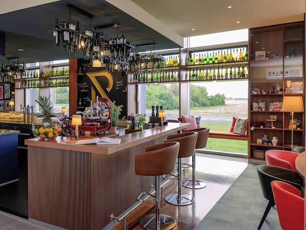 A modern bar area with a wooden counter, bar stools, and a view of the outdoors. - Mercure Hotel Frankfurt Eschborn Helfmann-Park (Eschborn)