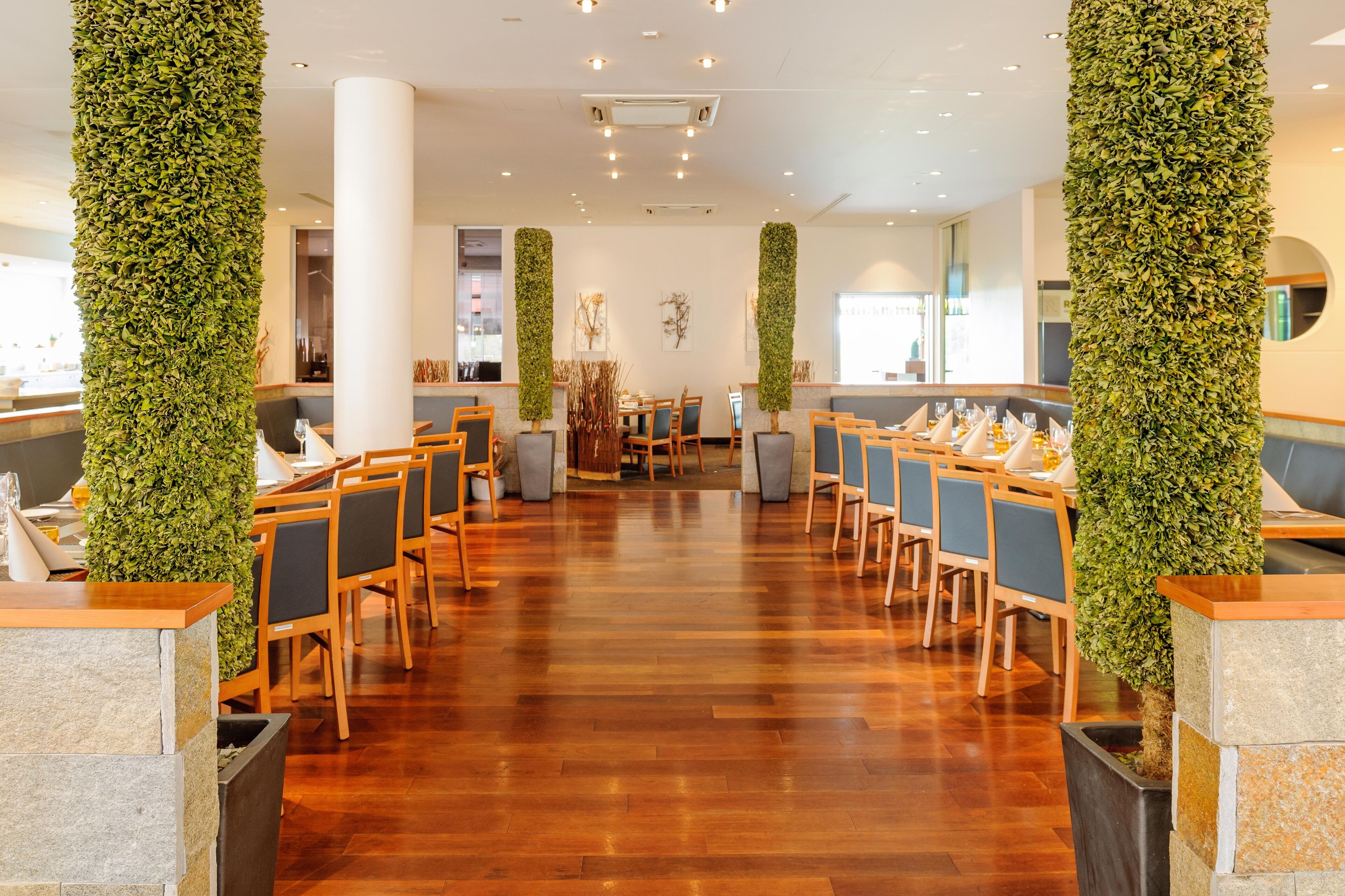 A spacious indoor area with wooden flooring, multiple seating arrangements, and vertical greenery accents.