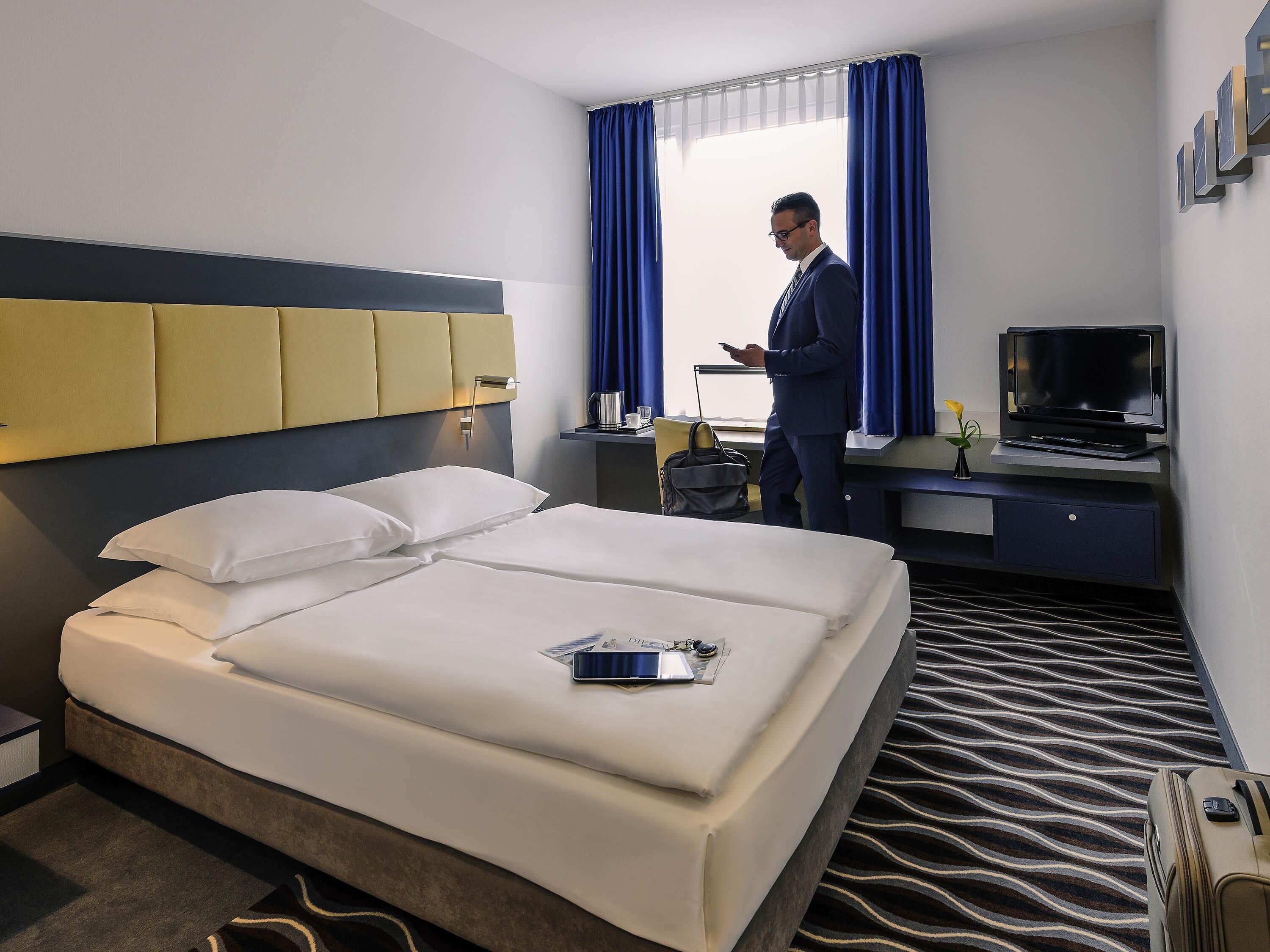 Una camera d'albergo con un letto, una scrivania con televisore e una finestra con tende.