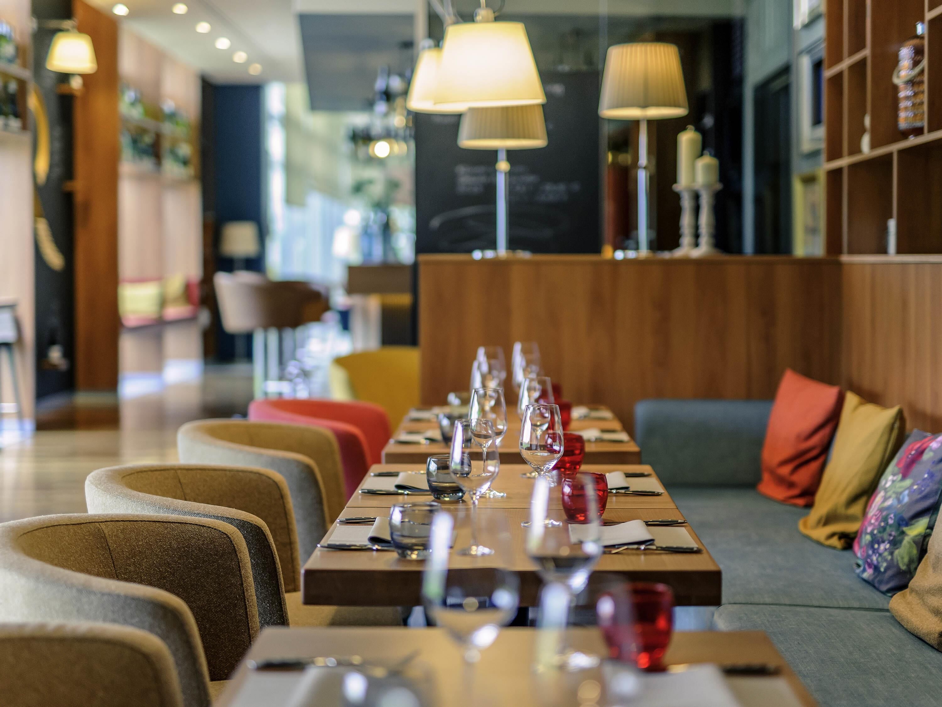 Ein Restaurant mit einem langen Esstisch, Stühlen und einer Couch mit Kissen.