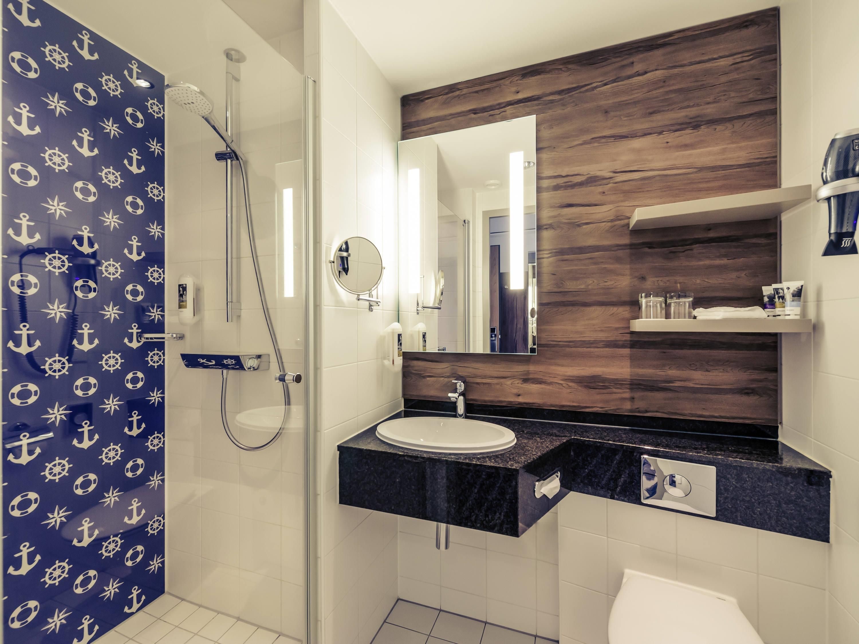 Une salle de bain moderne avec une douche à parois de verre, un miroir rond et un plan de toilette en marbre foncé.