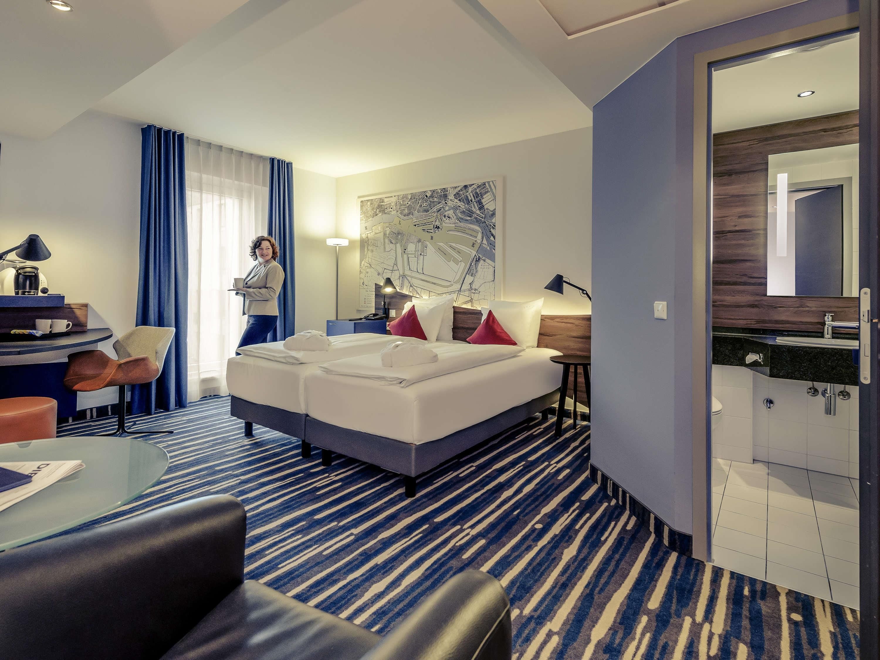 Una habitación de hotel con cama, escritorio y silla, una mesita y un baño con espejo.