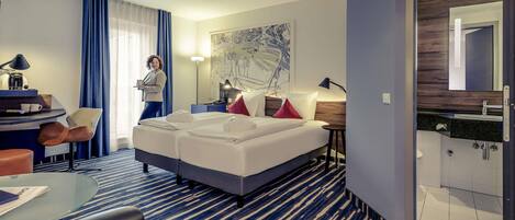 Una habitación de hotel con cama, escritorio y silla, una mesita y un baño con espejo.