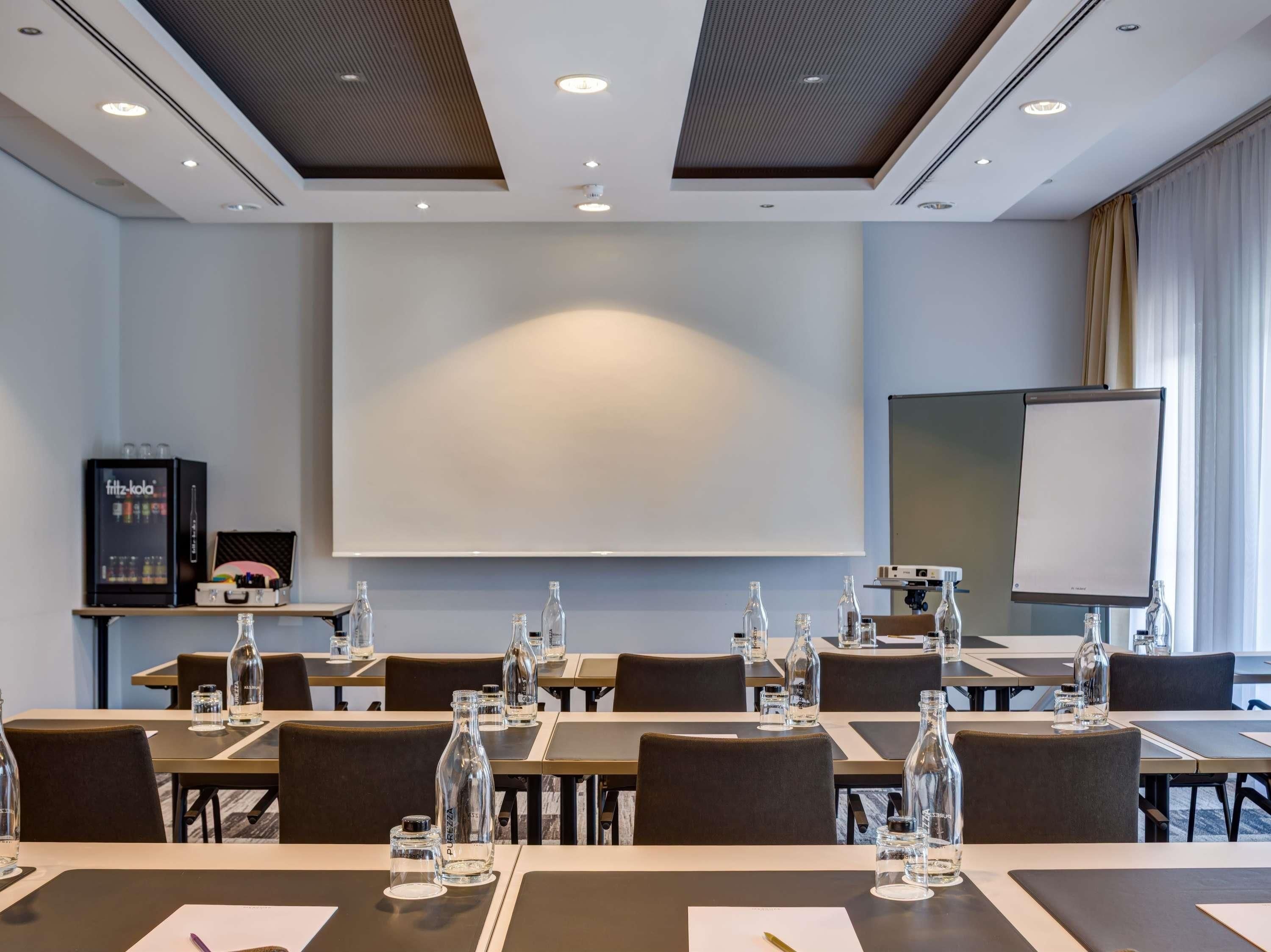 A conference room with tables set for meetings, a projector screen, and a whiteboard.