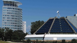 Un bâtiment moderne doté d’une façade incurvée et d’une structure en forme de pyramide, recouverte de panneaux solaires.