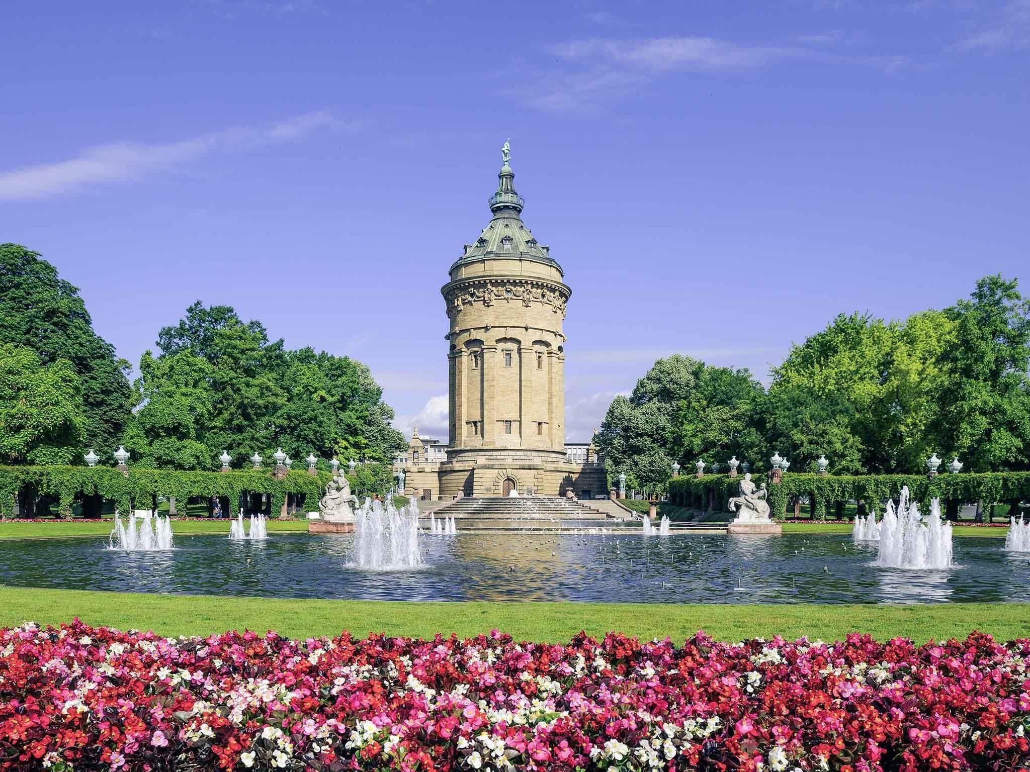 Una torre histórica con cúpula, rodeada de un jardín bien cuidado con fuentes y parterres de flores.