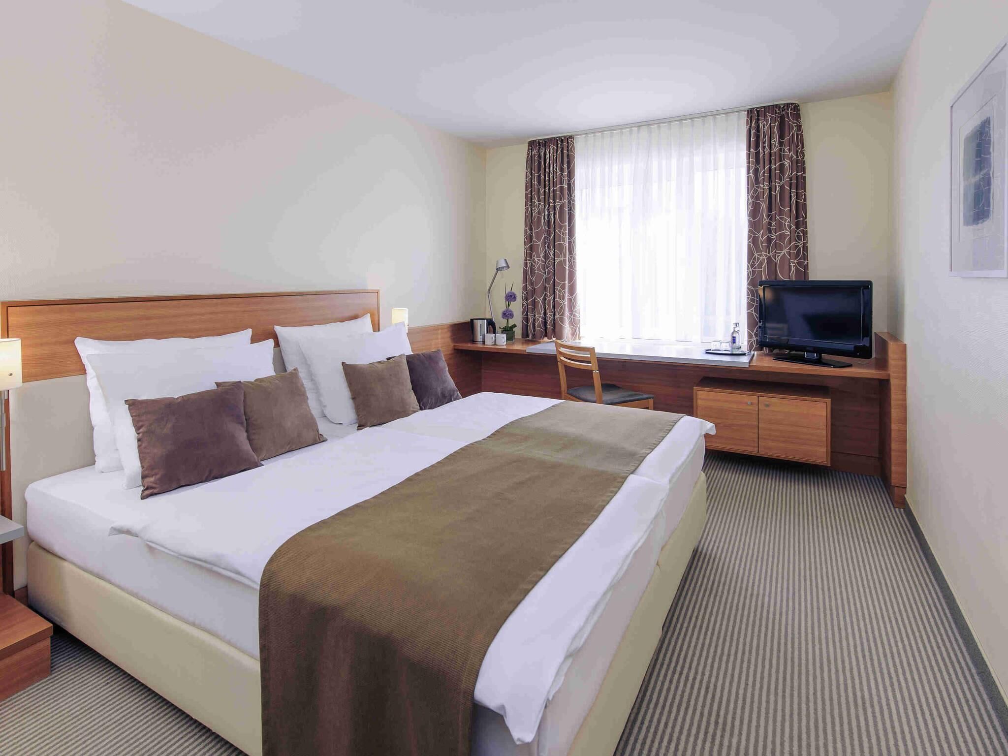 Una habitación de hotel con una cama, un escritorio con televisor, una silla y una lámpara.